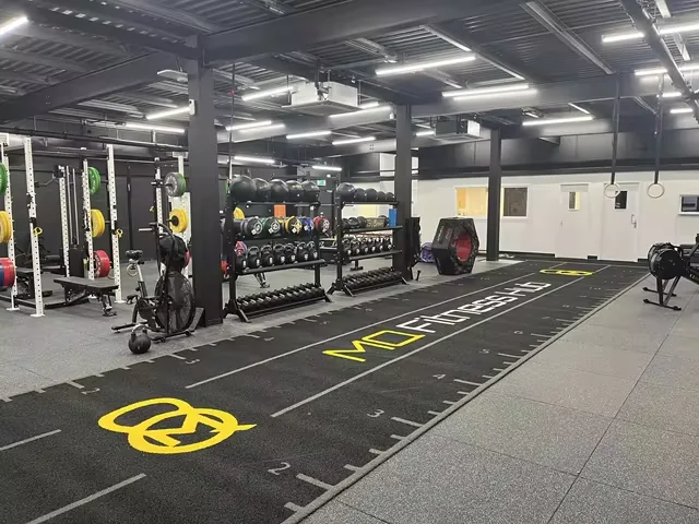 Wide view of black custom gym turf installed beside kettlebells and strength racks in a UK gym